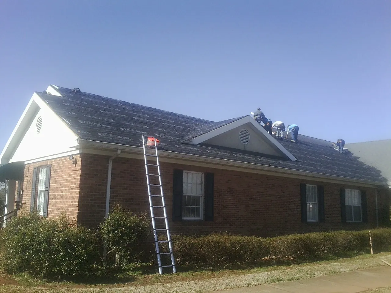 Crew tearing shingles off a brick ranch roof with a ladder set — Metal Roof Repair work by our crew in Suwannee