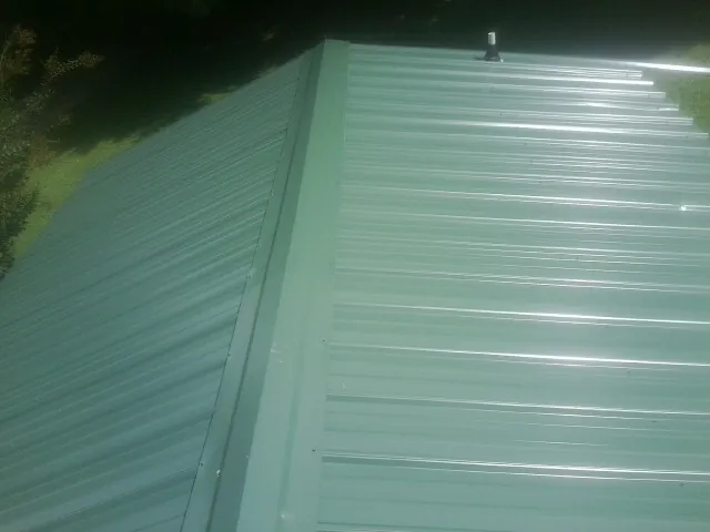 New green metal panels meeting at the ridge of a roof — Flat Roof Repair work by our crew in Suwannee