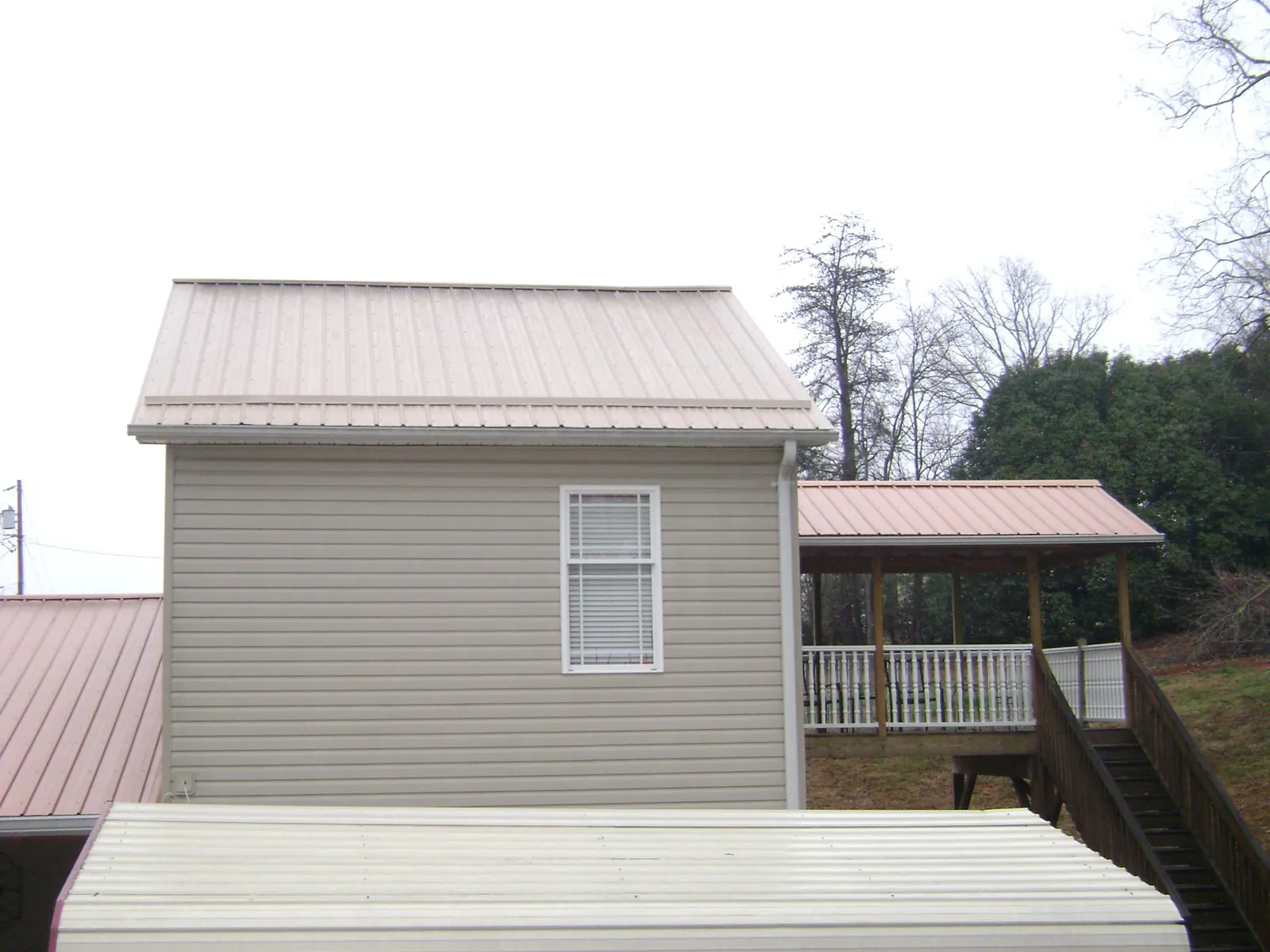 Tan metal roofs on a two story addition and attached porch, from a Roof Replacement job in Suwannee